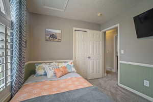 Carpeted bedroom with baseboards, visible vents, attic access, and a closet