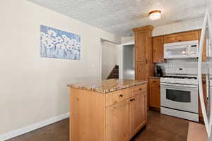 Kitchen with Alder cabinets, granite counters, a kitchen island, and white appliances