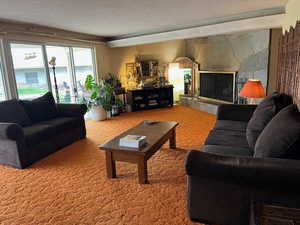 Carpeted living area featuring a textured ceiling and a fireplace with raised hearth