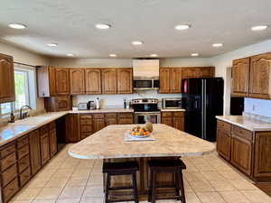 Kitchen with light tile patterned floors, brown cabinets, a sink, light countertops, and black appliances