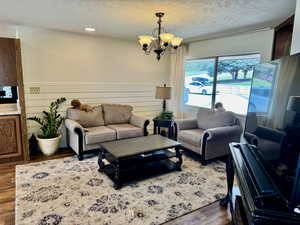 Living room with wood finished floors, a chandelier, a wainscoted wall, and a textured ceiling