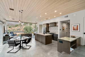 Kitchen featuring stainless steel appliances, finished concrete flooring, an island with sink, and light countertops