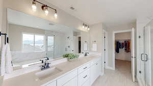 Full Primary bathroom featuring a walk in closet, a stall shower, double vanity, and a sink