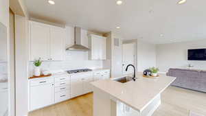 Kitchen with a sink, visible vents, open floor plan, wall chimney exhaust hood, and stainless steel gas cooktop