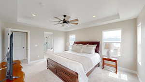 Bedroom featuring light colored carpet, visible vents, a raised ceiling, and baseboards