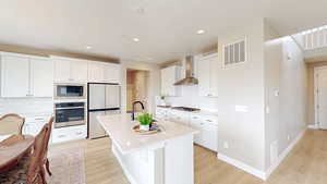Kitchen featuring a sink, appliances with stainless steel finishes, visible vents, wall chimney exhaust hood, and a kitchen island with sink