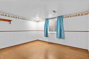 Empty room with a textured ceiling, visible vents, wood finished floors, and baseboards