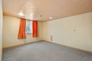 Carpeted spare room with a textured ceiling, visible vents, and baseboards
