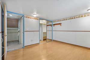 Unfurnished bedroom featuring a textured ceiling, wood finished floors, baseboards, and wainscoting