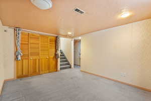 Finished below grade area featuring stairs, carpet flooring, a textured ceiling, and visible vents