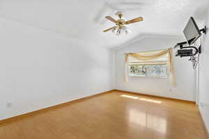 Empty master bedroom featuring a ceiling fan, baseboards, vaulted ceiling, and light wood-style floors