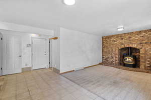 Unfurnished living room with tile patterned floors, carpet flooring, baseboards, visible vents, and a wood stove