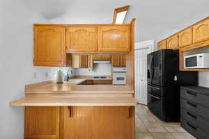 Kitchen featuring a sink, under cabinet range hood, a peninsula, white appliances, and lofted ceiling