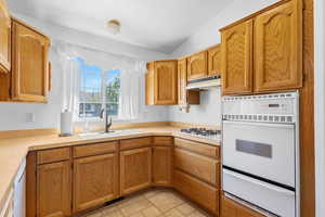 Kitchen featuring a sink, light countertops, under cabinet range hood, a warming drawer, and white appliances
