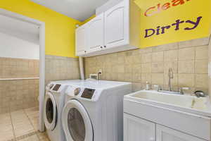 Laundry area featuring light tile patterned flooring, washer and clothes dryer, cabinet space, and tile walls