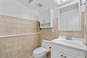 Bathroom featuring toilet, tile walls, visible vents, and vanity off of laundry room.