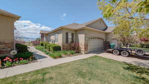 View of side of property featuring stucco siding, driveway, stone siding, a lawn, and a garage