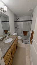Basement 3/4 bathroom with a shower stall, visible vents, toilet, vanity, and a textured ceiling