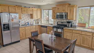 Basement kitchen with decorative backsplash, appliances with stainless steel finishes, a sink, and light tile patterned flooring