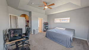 Primary bedroom featuring a tray ceiling, connected bathroom, arched walkways, baseboards, and ceiling fan