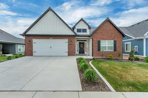 View of front of house with an attached garage, brick siding, board and batten siding, and driveway