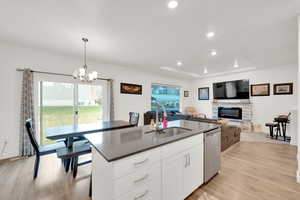 Kitchen featuring stainless steel dishwasher, light wood finished floors, a sink, and a fireplace