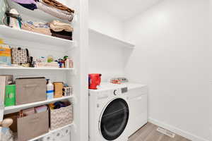 Laundry room with laundry area, light wood finished floors, separate washer and dryer, baseboards, and visible vents