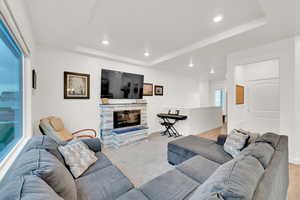 Living room with recessed lighting, a tray ceiling, and a stone fireplace
