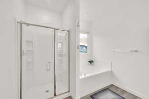 Bathroom featuring wood finished floors, a garden tub, a stall shower, and baseboards