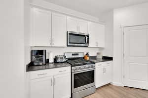 Kitchen with dark countertops, white cabinets, stainless steel appliances, and light wood-style floors