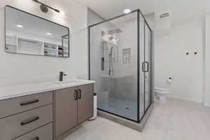 Bathroom featuring a stall shower, wood finished floors, toilet, and vanity
