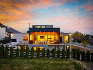 Back of property at dusk with fence, a balcony, and a yard