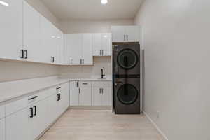 Laundry room featuring recessed lighting, cabinet space, a sink, light wood-type flooring, and stacked washer and clothes dryer