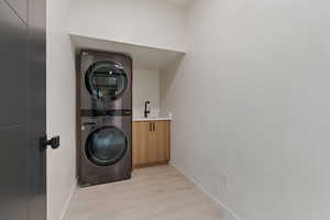 Clothes washing area with light wood finished floors, cabinet space, stacked washer and clothes dryer, and baseboards