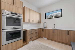 Kitchen with light wood-style flooring, light countertops, double oven, a sink, and visible vents