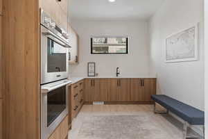 Kitchen with a sink, modern cabinets, stainless steel double oven, light wood-type flooring, and light countertops