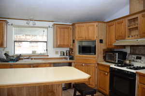 Kitchen with stainless steel microwave, gas range, under cabinet range hood, light countertops, and a sink