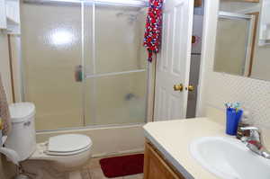 Full bath featuring vanity, toilet, tile patterned flooring, and enclosed tub / shower combo