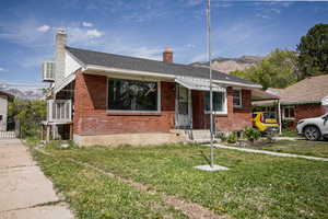 View of front of home with a chimney, brick siding, an attached carport, a mountain view, and a front lawn