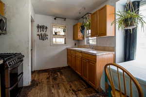 Kitchen featuring appliances with stainless steel finishes, light countertops, brown cabinets, a sink, and dark wood-type flooring