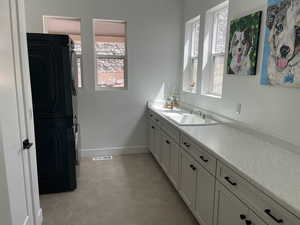 Bathroom featuring stacked washer and clothes dryer, visible vents, baseboards, tile patterned floors, and vanity