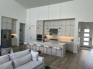 Kitchen featuring high end fridge, under cabinet range hood, a sink, open floor plan, and a towering ceiling