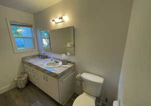 Half bathroom with wood finished floors, toilet, vanity, baseboards, and a textured ceiling
