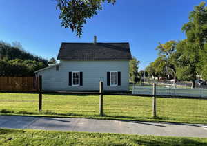 View of property exterior featuring a chimney, fence, roof with shingles, and a lawn