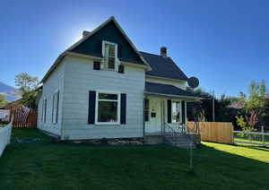 View of front of property featuring a chimney, fence, a front lawn, and roof with shingles