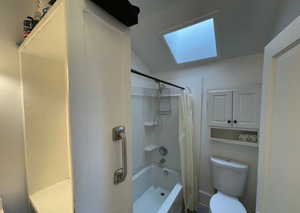 Full bath featuring shower / bathtub combination with curtain, toilet, and vaulted ceiling with skylight