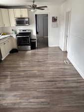 Kitchen with stainless steel appliances, ceiling fan, cream cabinets, and dark wood-type flooring