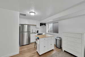 Kitchen featuring light wood finished floors, visible vents, white cabinetry, appliances with stainless steel finishes, and butcher block counters