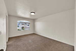 Spare room with a textured ceiling, dark carpet, and baseboards