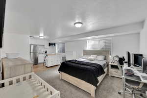 Bedroom with a textured ceiling, light wood finished floors, and freestanding refrigerator